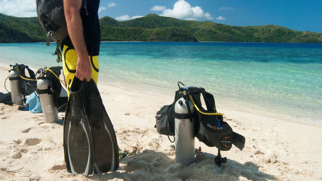 Diver on beach with equipment at Barefoot Manta Resort – a great place to learn to dive in the Yasawa Islands Fiji